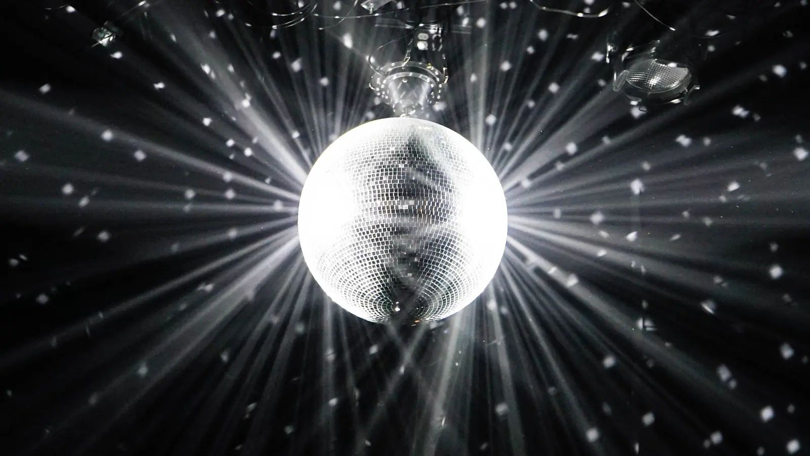 Illustrative photo, not The Grand Palace KTV: Mirror disco ball with radiating light beams on a black background (black and white)